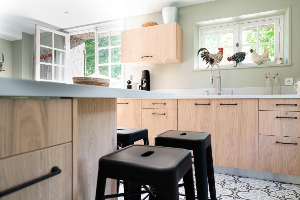 Réalisation d'une grande cuisine design en bois clair fermée avec un évier intégré, un placard à porte plane, un plan de travail en surface solide, une crédence grise, un électroménager en acier inoxydable, carreaux de ciment au sol, une péninsule, un sol beige et un plan de travail gris.