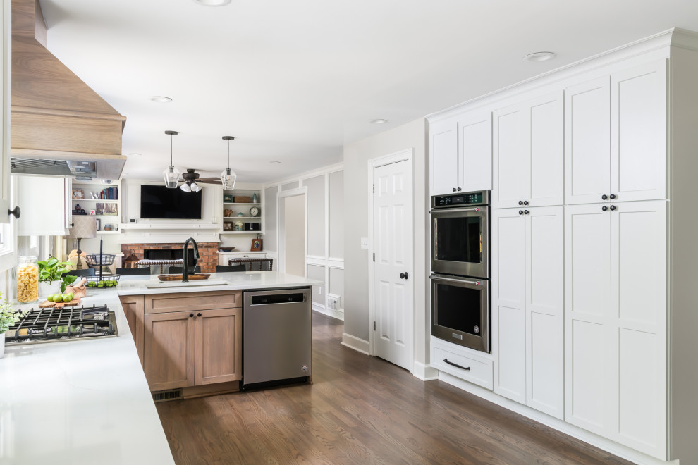 Photo of a mid-sized country open plan kitchen in Atlanta with an undermount sink, shaker cabinets, medium wood cabinets, quartz benchtops, white splashback, ceramic splashback, stainless steel appliances, medium hardwood floors, a peninsula, brown floor and white benchtop.