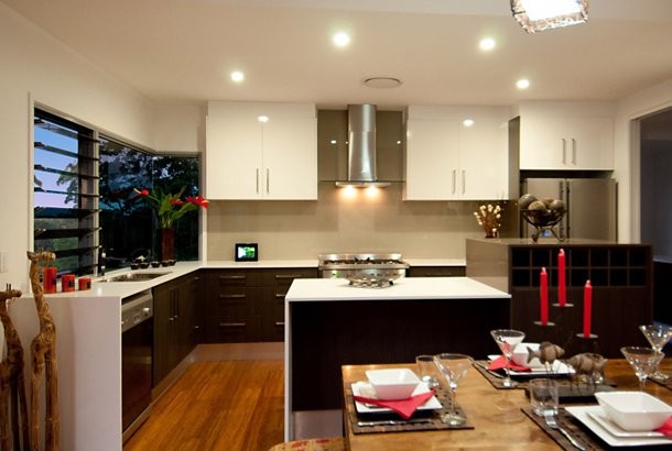 Photo of a mid-sized asian l-shaped kitchen in Sunshine Coast with a double-bowl sink, flat-panel cabinets, dark wood cabinets, solid surface benchtops, beige splashback, glass sheet splashback, stainless steel appliances, bamboo floors and with island.