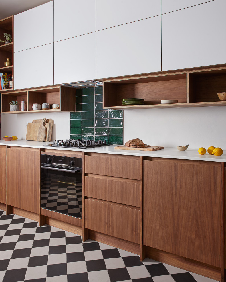 Inspiration for a contemporary kitchen in Devon with flat-panel cabinets, medium wood cabinets, green splashback, subway tile splashback, black appliances, multi-coloured floor and white benchtop.