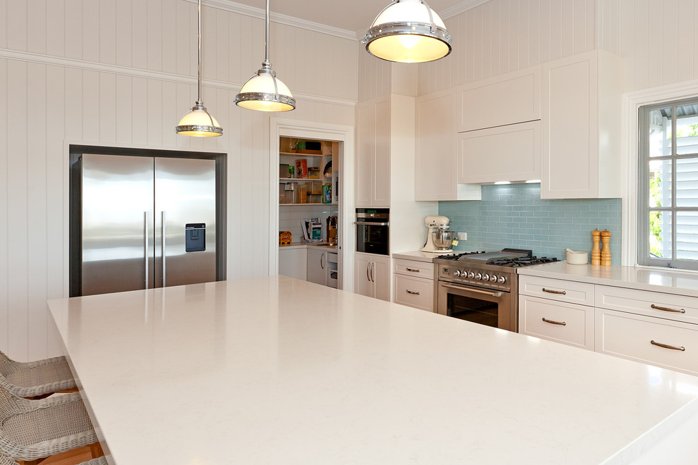 Inspiration for a large traditional l-shaped kitchen pantry in Brisbane with shaker cabinets, white cabinets, blue splashback, stainless steel appliances, light hardwood floors and with island.