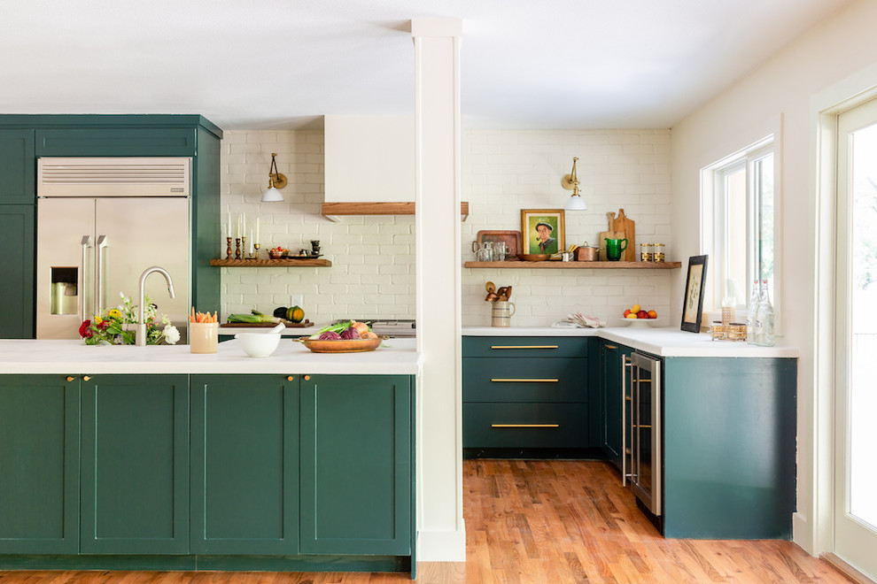 Inspiration for a mid-sized transitional l-shaped kitchen in Dallas with shaker cabinets, green cabinets, white splashback, brick splashback, stainless steel appliances, medium hardwood floors, with island, brown floor and white benchtop.