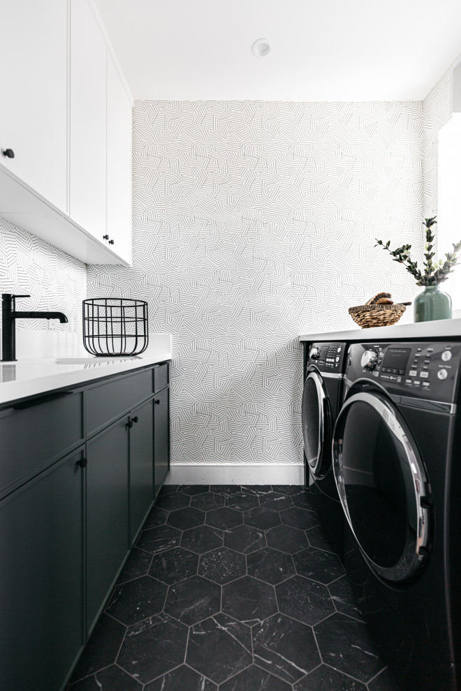 Inspiration for a small country galley dedicated laundry room in Los Angeles with quartz benchtops, porcelain floors, a side-by-side washer and dryer, black floor, white benchtop, an undermount sink, flat-panel cabinets, black cabinets, white walls and wallpaper.