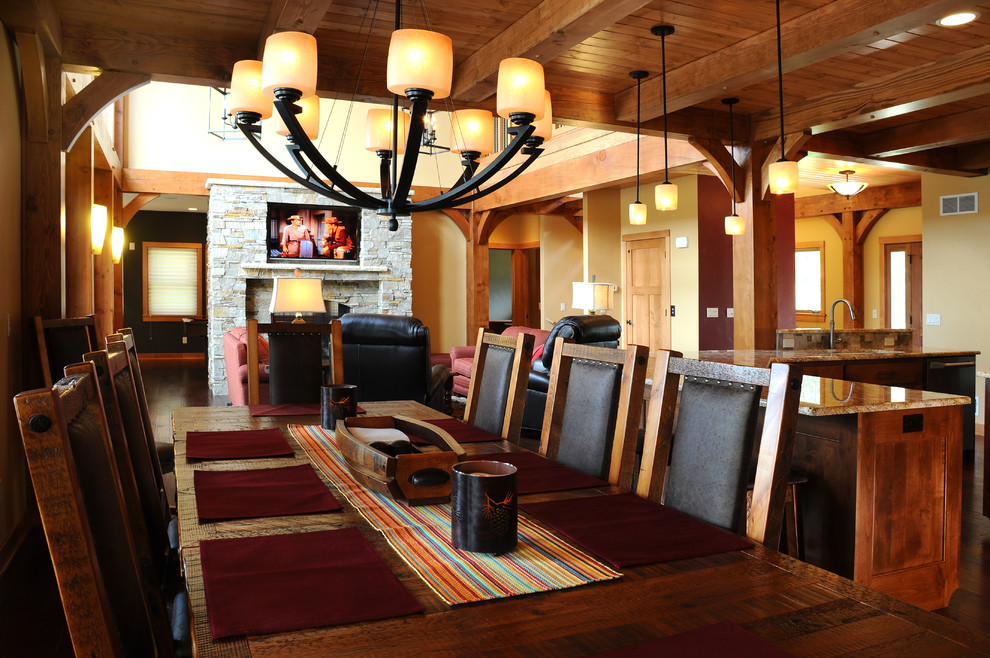 Mid-sized mountain style dark wood floor kitchen/dining room combo photo with beige walls, a standard fireplace and a stone fireplace