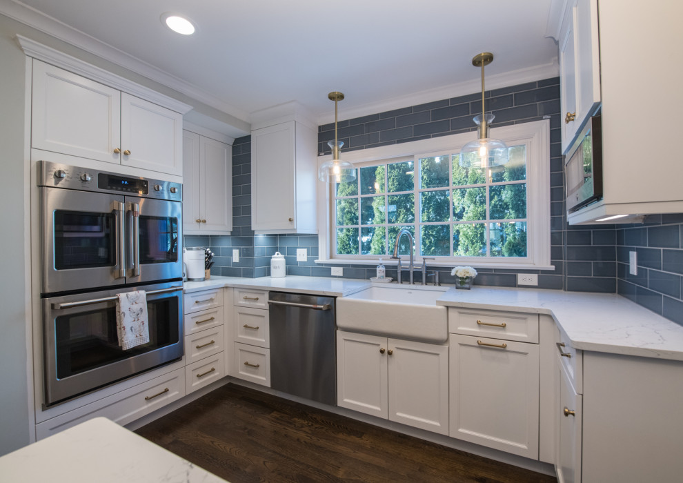 Example of a transitional dark wood floor and brown floor open concept kitchen design in Bridgeport with a farmhouse sink, white cabinets, quartz countertops, gray backsplash, ceramic backsplash, stainless steel appliances, an island and white countertops