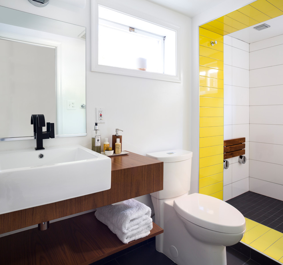 This is an example of a contemporary bathroom in DC Metro with flat-panel cabinets, brown cabinets, an open shower, a one-piece toilet, white tile, white walls, a vessel sink, wood benchtops and black floor.