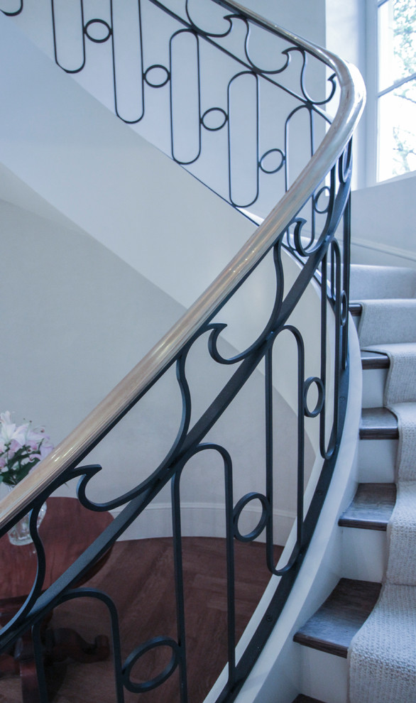 Example of a large transitional wooden curved metal railing staircase design in DC Metro with wooden risers