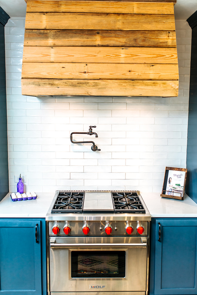 This is an example of a large country l-shaped eat-in kitchen in Austin with a farmhouse sink, shaker cabinets, blue cabinets, granite benchtops, white splashback, subway tile splashback, stainless steel appliances, bamboo floors, with island, brown floor and white benchtop.