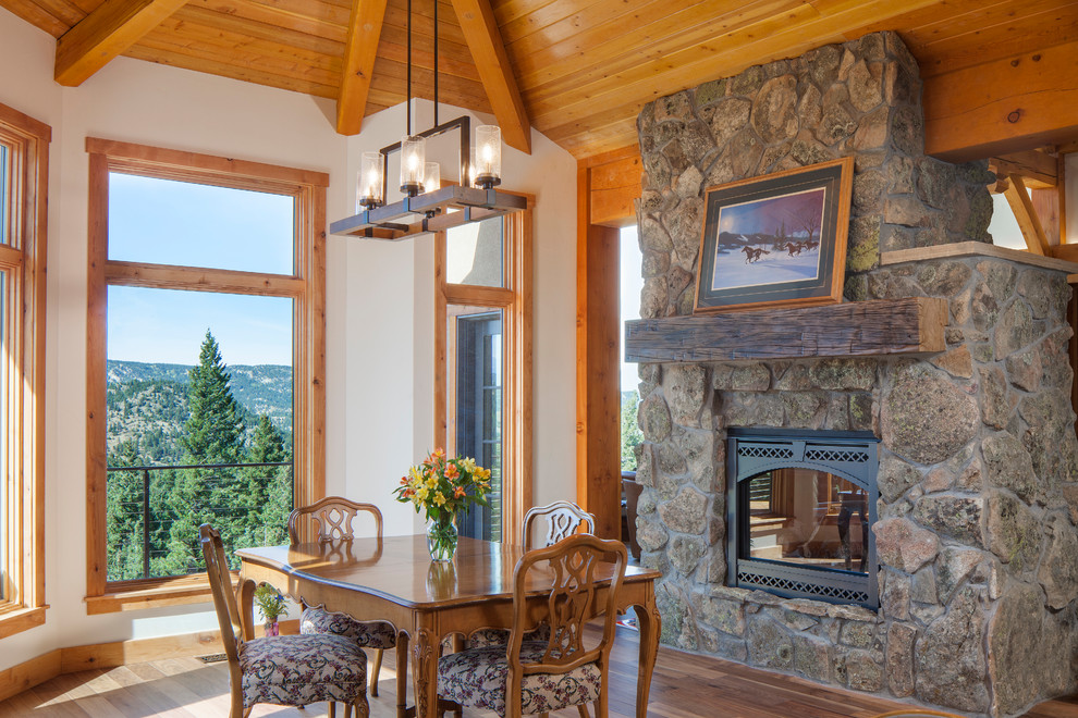 Photo of a country dining room in Denver with a two-sided fireplace, a stone fireplace surround, white walls, brown floor and dark hardwood floors.