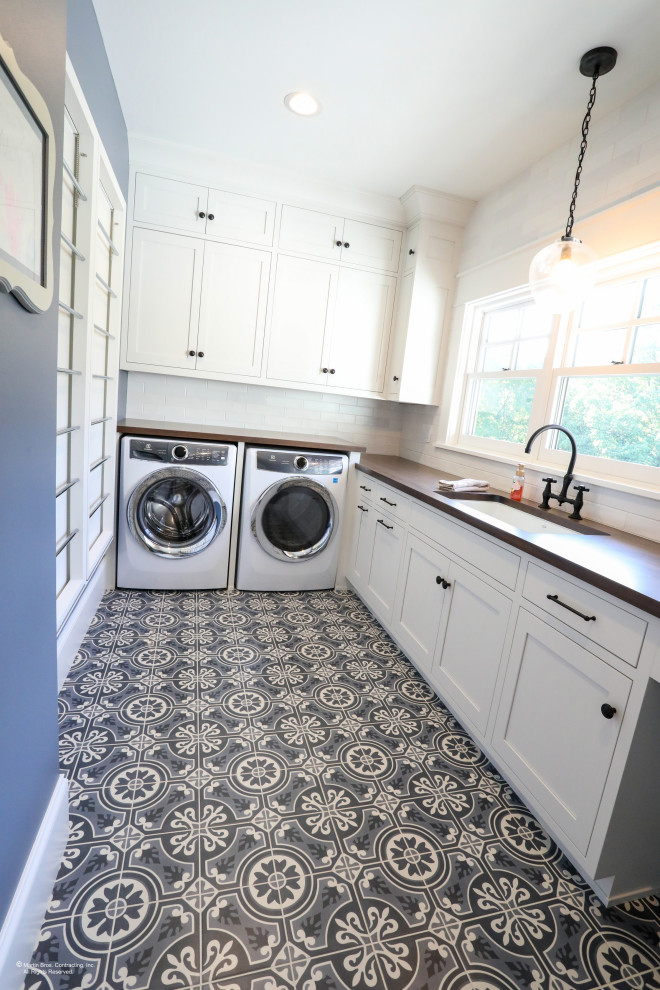 Inspiration for a large transitional u-shaped dedicated laundry room in Other with a farmhouse sink, shaker cabinets, white cabinets, wood benchtops, white splashback, ceramic splashback, blue walls, ceramic floors, an integrated washer and dryer and grey floor.