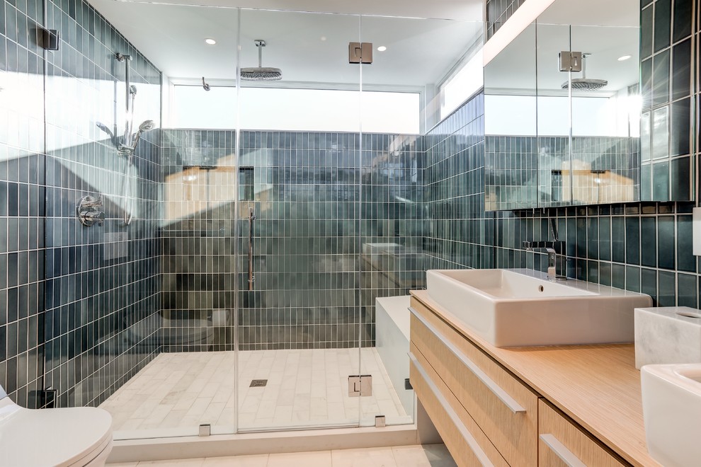 This is an example of a contemporary master bathroom in New York with flat-panel cabinets, light wood cabinets, an alcove shower, a vessel sink, wood benchtops, a hinged shower door, a freestanding tub, a wall-mount toilet, blue tile, ceramic tile, blue walls, marble floors and white floor.