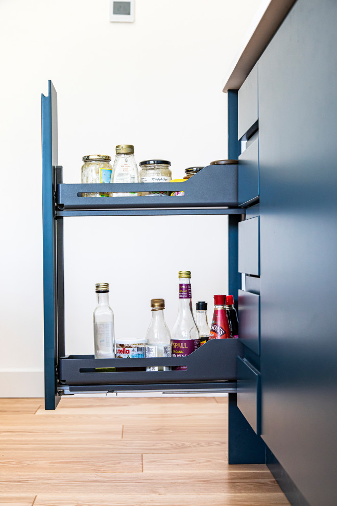 Immagine di una cucina minimalista di medie dimensioni con ante lisce, ante blu, top in quarzo composito, paraspruzzi bianco, paraspruzzi con lastra di vetro, nessuna isola e top bianco