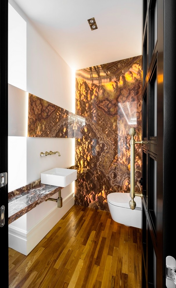 Mid-sized transitional powder room in Madrid with a wall-mount toilet, orange tile, marble, white walls, medium hardwood floors, a vessel sink, onyx benchtops and brown floor.