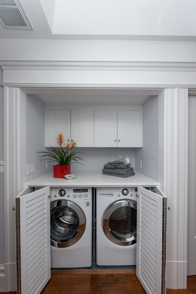 Design ideas for a mid-sized transitional single-wall laundry cupboard in San Francisco with louvered cabinets, white cabinets, blue walls, a side-by-side washer and dryer, grey floor and white benchtop.