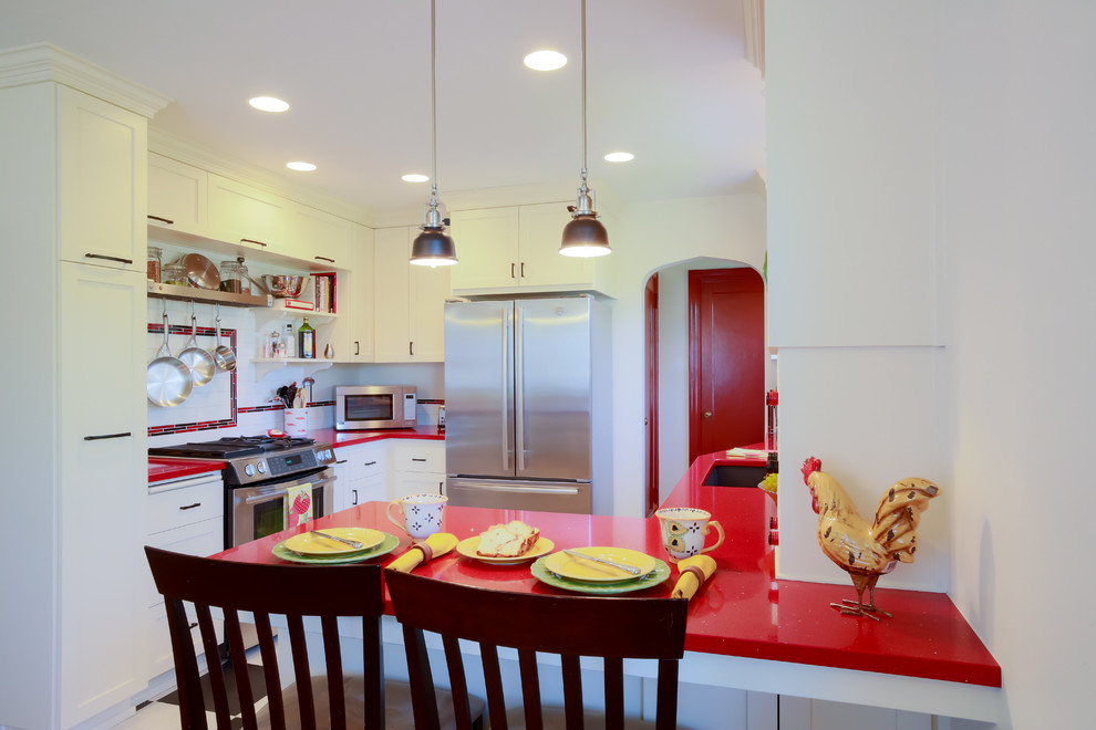 This is an example of a small eclectic l-shaped eat-in kitchen in Portland with an undermount sink, white splashback, subway tile splashback, stainless steel appliances, white cabinets, shaker cabinets, solid surface benchtops, a peninsula, black floor, red benchtop and vinyl floors.