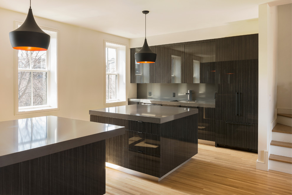 This is an example of a large modern u-shaped eat-in kitchen in Boston with a drop-in sink, flat-panel cabinets, black cabinets, quartz benchtops, black splashback, stone slab splashback, panelled appliances, medium hardwood floors and multiple islands.