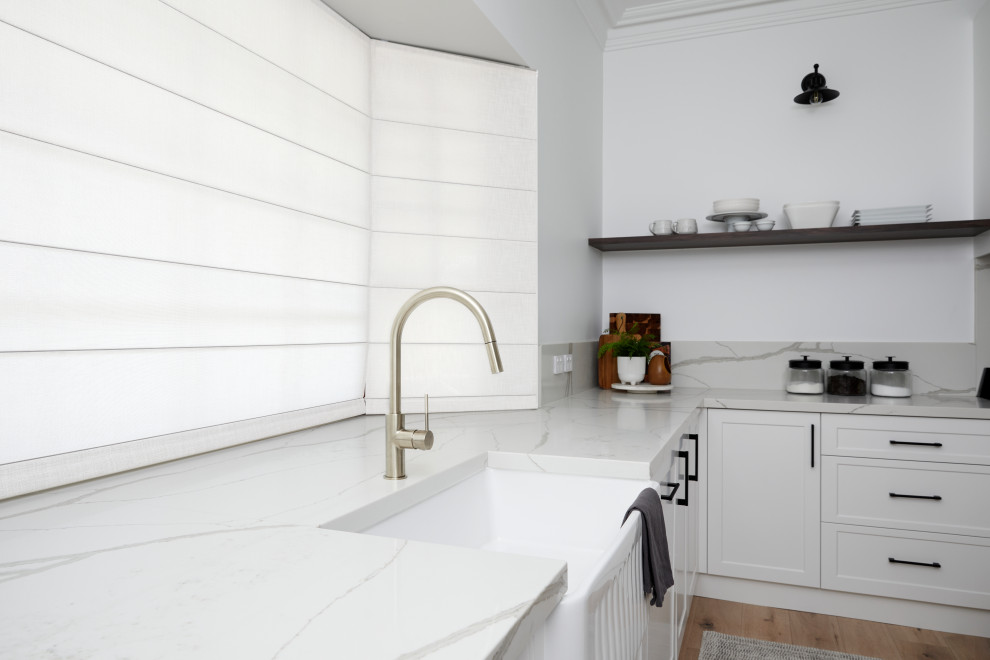 Photo of a shabby-chic style eat-in kitchen in Sydney with a farmhouse sink, quartz benchtops, white splashback, engineered quartz splashback, white appliances, light hardwood floors, with island, beige floor and white benchtop.