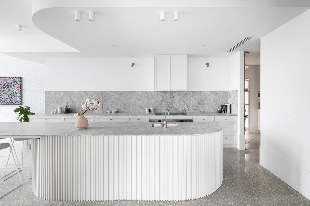 Photo of a large contemporary galley open plan kitchen in Melbourne with shaker cabinets, grey splashback, concrete floors, with island, grey benchtop, an undermount sink, white cabinets and grey floor.