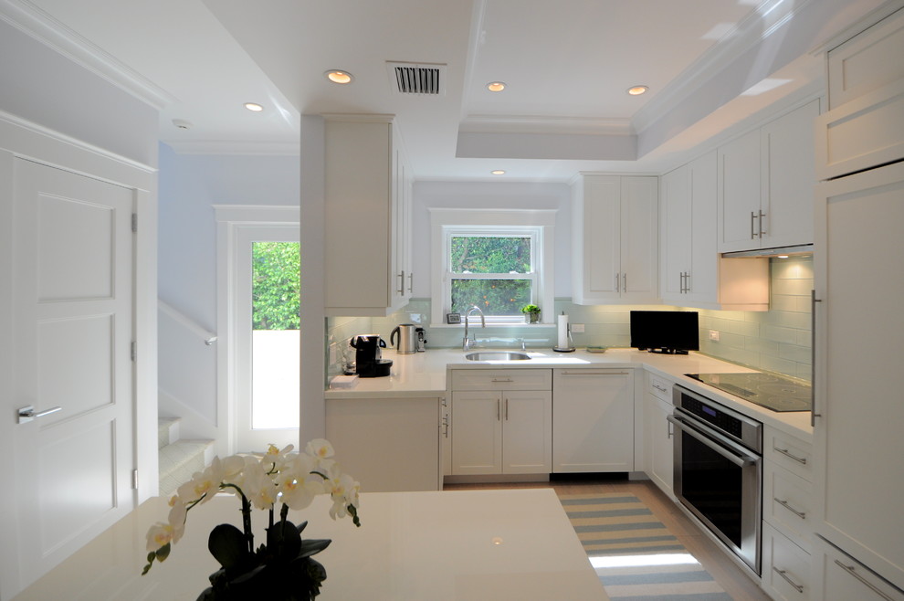 This is an example of a mid-sized beach style l-shaped eat-in kitchen in Miami with an undermount sink, shaker cabinets, white cabinets, recycled glass benchtops, green splashback, glass tile splashback, stainless steel appliances, light hardwood floors and with island.