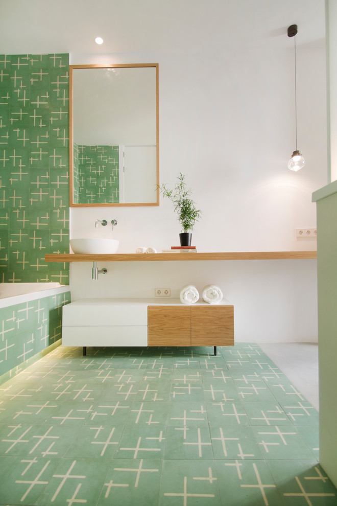 Photo of a contemporary master bathroom in Madrid with open cabinets, medium wood cabinets, a drop-in tub, green tile, a vessel sink, wood benchtops, green floor, white walls and beige benchtops.