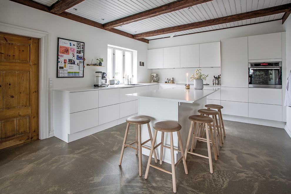 This is an example of a large contemporary l-shaped eat-in kitchen in Aarhus with flat-panel cabinets, white cabinets, white splashback, panelled appliances, concrete floors and with island.