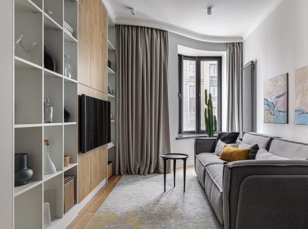 Esempio di un piccolo soggiorno design con libreria, pareti bianche, pavimento in legno massello medio e TV a parete