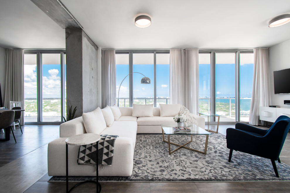 Photo of a contemporary open concept living room in Miami with white walls, a wall-mounted tv and brown floor.