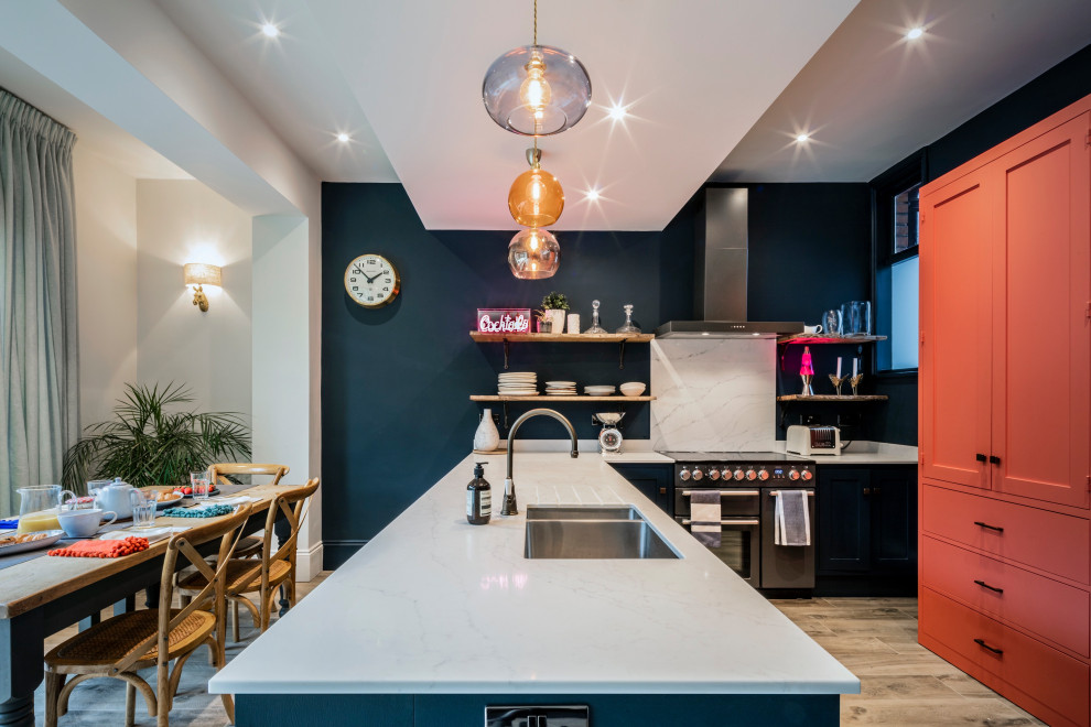 Design ideas for a mid-sized eclectic l-shaped open plan kitchen in Kent with a drop-in sink, shaker cabinets, blue cabinets, solid surface benchtops, white splashback, coloured appliances, ceramic floors, with island, beige floor and white benchtop.