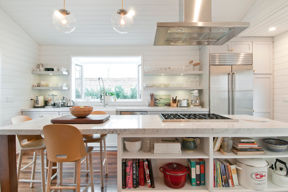Mid-sized country galley eat-in kitchen in Los Angeles with a farmhouse sink, shaker cabinets, white cabinets, white splashback, with island, marble benchtops, timber splashback, stainless steel appliances and painted wood floors.
