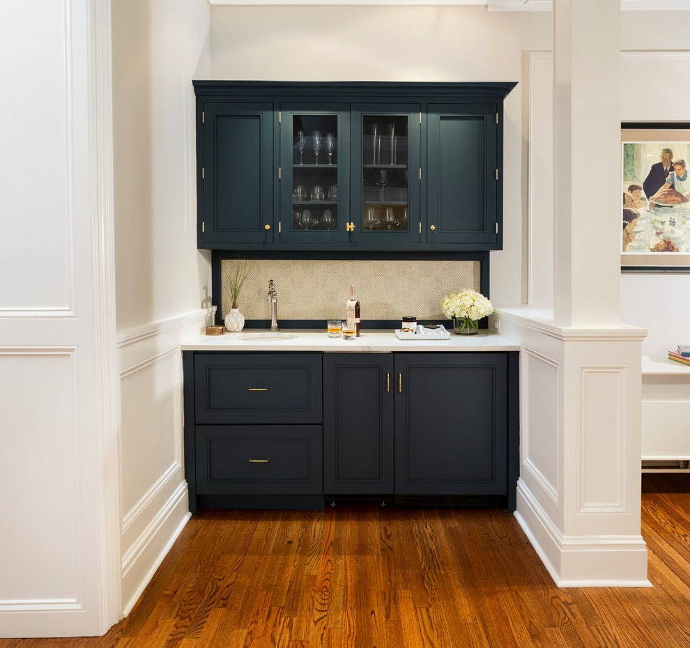 This is an example of a transitional single-wall wet bar in Philadelphia with quartzite benchtops, medium hardwood floors, an undermount sink, glass-front cabinets, blue cabinets, beige splashback and brown floor.