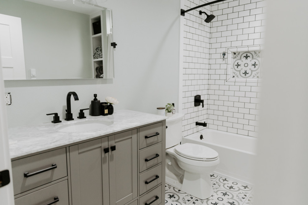 Cette image montre une petite salle de bain rustique avec un placard à porte shaker, des portes de placard grises, une baignoire en alcôve, un carrelage blanc, des carreaux de céramique, un mur vert, un sol en carrelage de porcelaine, un lavabo encastré, un plan de toilette en marbre, un sol gris, une cabine de douche avec un rideau, un plan de toilette blanc, des toilettes cachées, meuble simple vasque et meuble-lavabo sur pied.
