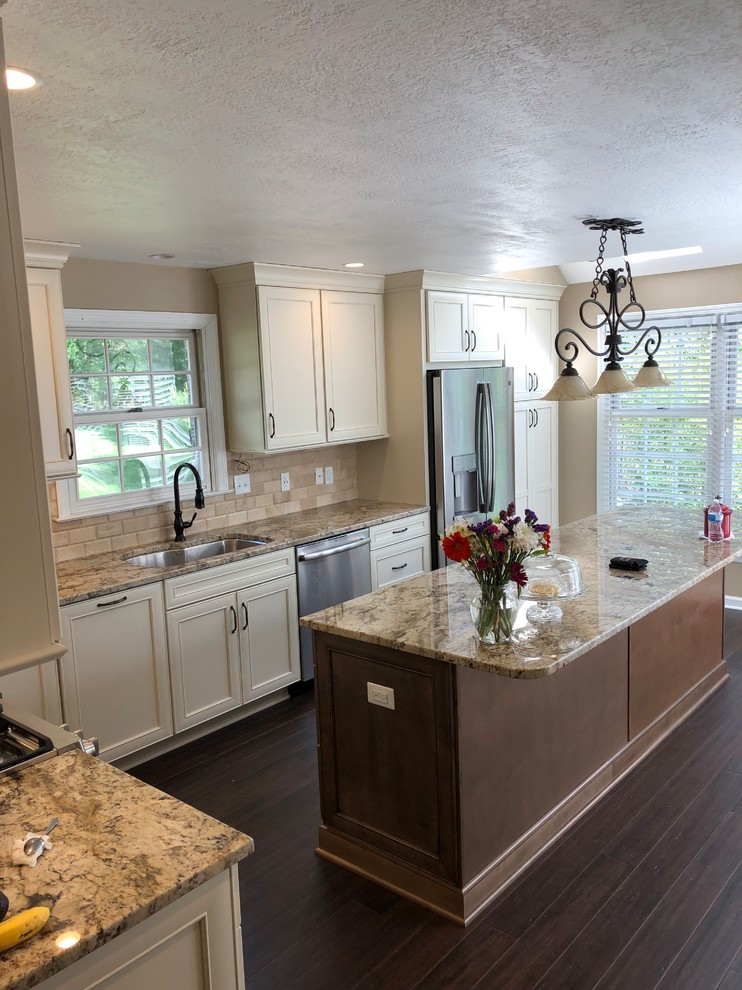 Inspiration for a modern dark wood floor and brown floor kitchen remodel with an undermount sink, recessed-panel cabinets, beige cabinets, granite countertops, beige backsplash, stone tile backsplash, stainless steel appliances, an island and multicolored countertops