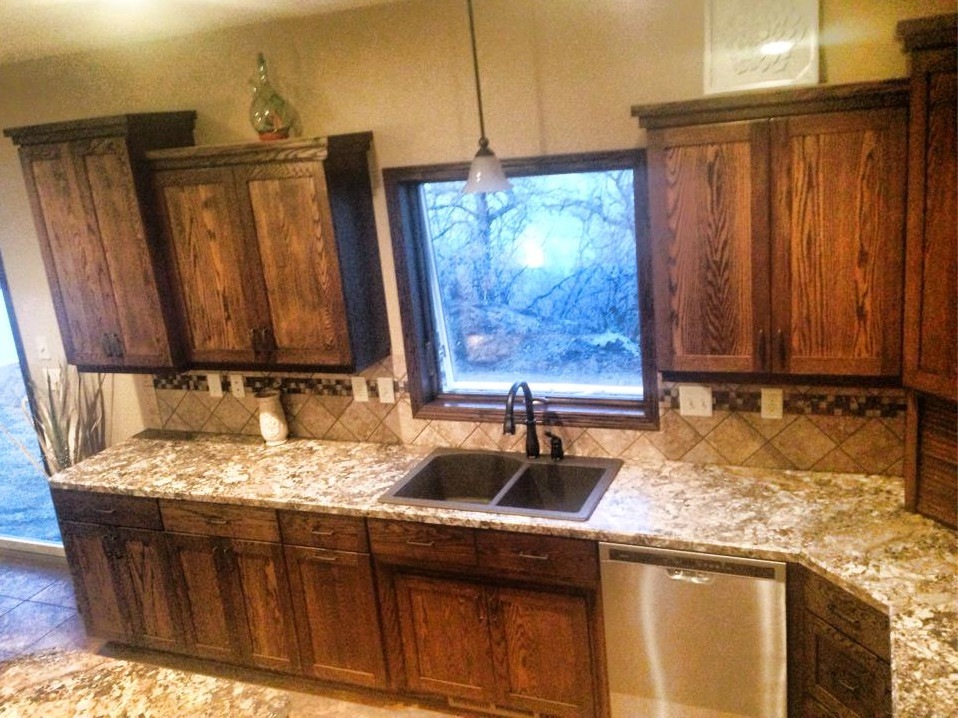 Mid-sized mountain style l-shaped laminate floor and beige floor eat-in kitchen photo with a drop-in sink, recessed-panel cabinets, dark wood cabinets, granite countertops, beige backsplash, ceramic backsplash, stainless steel appliances and an island