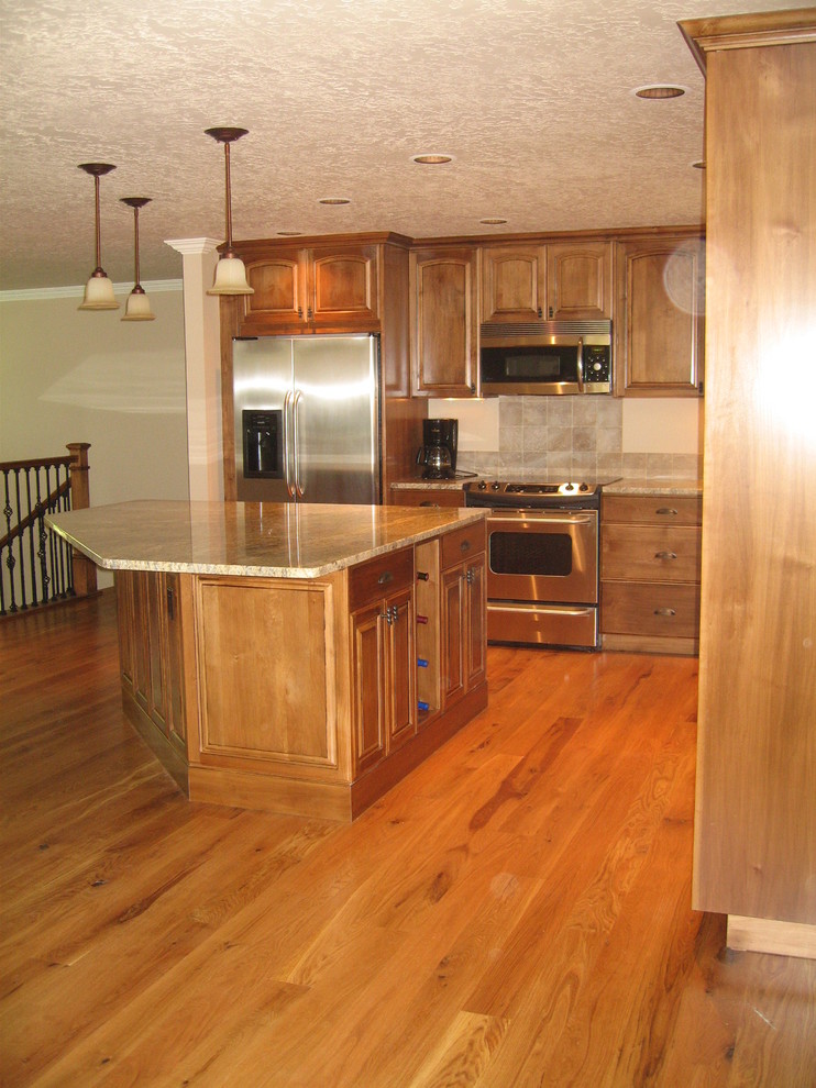 This is an example of a mid-sized traditional l-shaped eat-in kitchen in Boise with an undermount sink, raised-panel cabinets, medium wood cabinets, granite benchtops, brown splashback, stone tile splashback, stainless steel appliances, medium hardwood floors and with island.