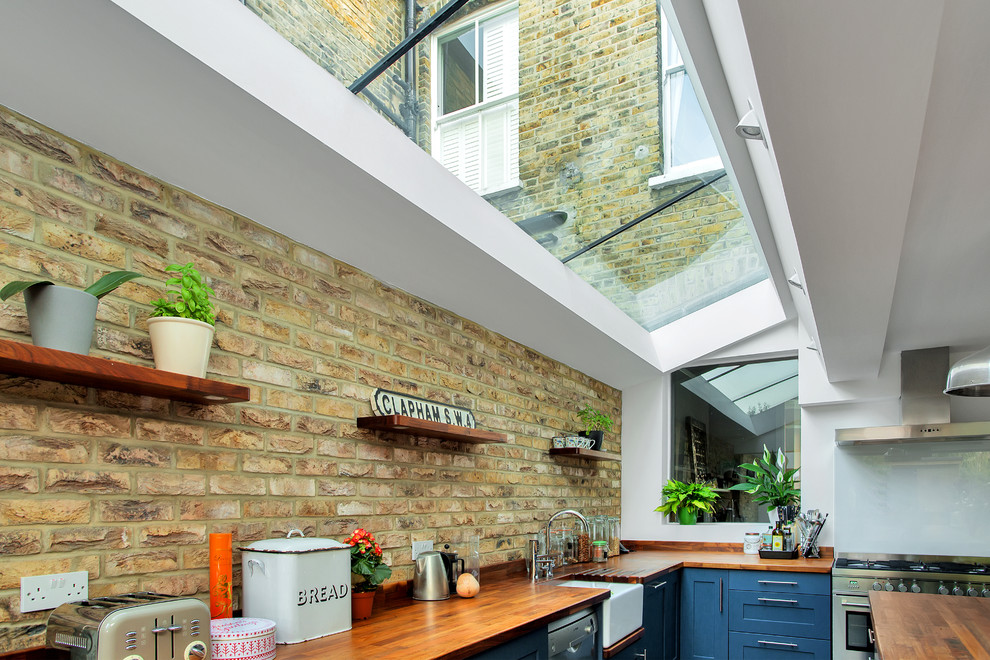 Inspiration for a large industrial eat-in kitchen in London with a farmhouse sink, shaker cabinets, blue cabinets, wood benchtops, white splashback, glass sheet splashback, stainless steel appliances, ceramic floors, with island, grey floor and brown benchtop.