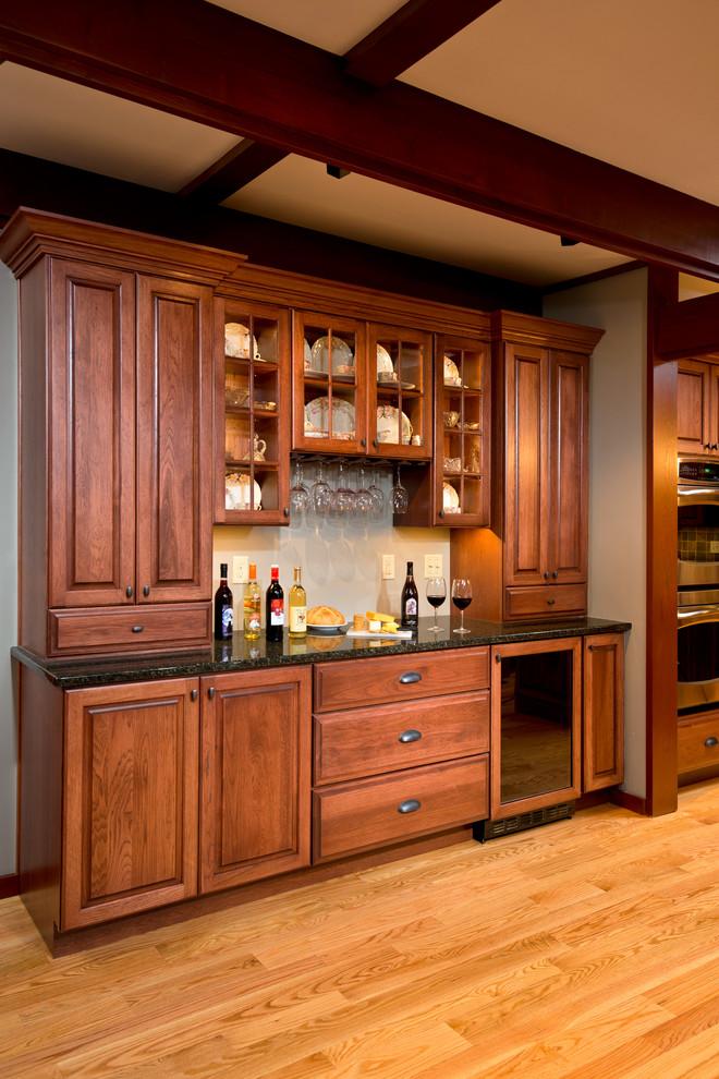 Mid-sized arts and crafts single-wall wet bar in Boston with no sink, raised-panel cabinets, medium wood cabinets, granite benchtops, light hardwood floors and brown floor.