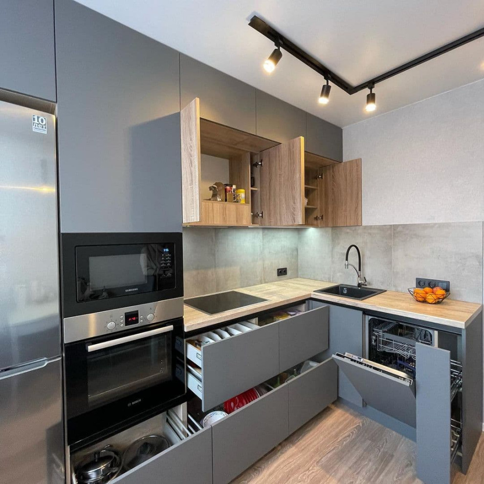 This is an example of a medium sized contemporary l-shaped kitchen/diner in Moscow with a built-in sink, flat-panel cabinets, green cabinets, wood worktops, grey splashback, porcelain splashback, black appliances, laminate floors, no island, brown floors and yellow worktops.