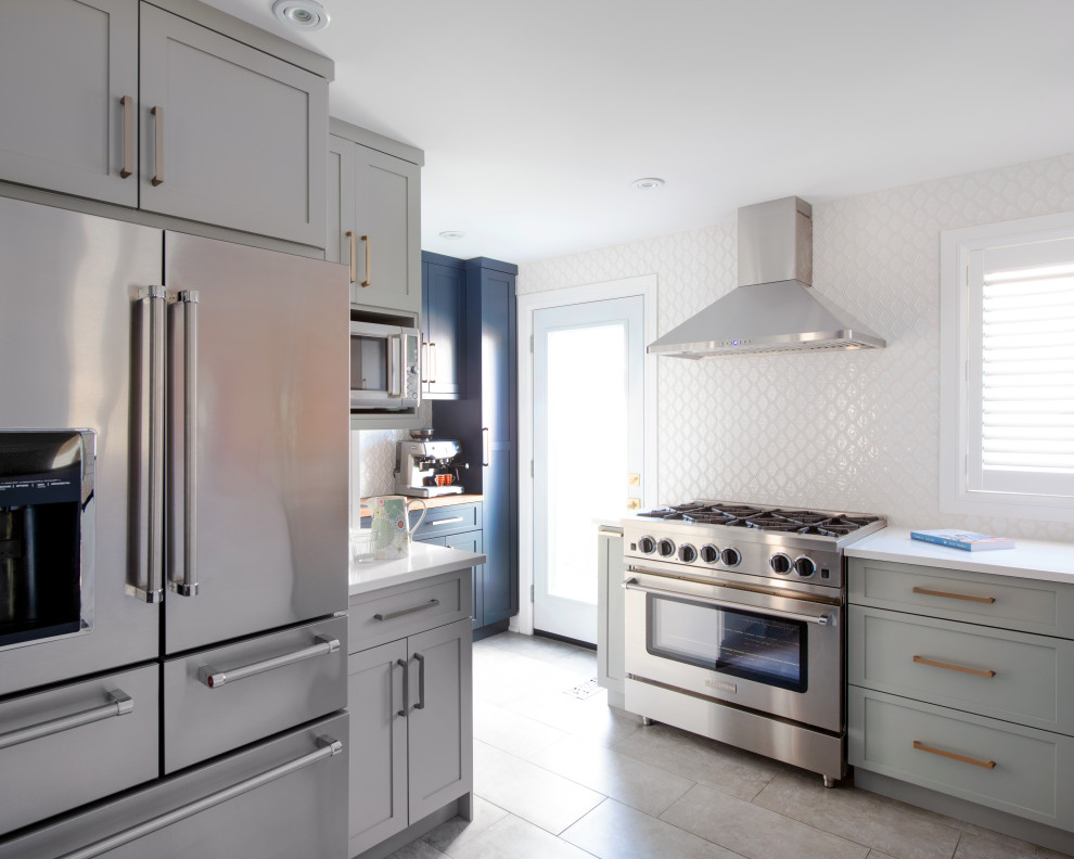 Example of a mid-sized transitional l-shaped ceramic tile kitchen design in Ottawa with a double-bowl sink, shaker cabinets, quartz countertops, white backsplash, stainless steel appliances, a peninsula and white countertops
