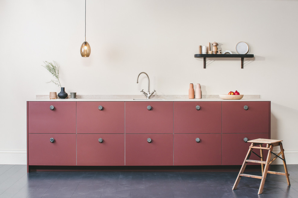 Design ideas for a small contemporary single-wall open plan kitchen in Other with a drop-in sink, flat-panel cabinets, red cabinets, solid surface benchtops, beige splashback, stone slab splashback, panelled appliances, painted wood floors, no island, black floor and beige benchtop.