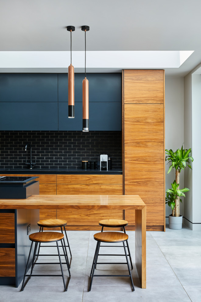 Photo of a contemporary kitchen in London with flat-panel cabinets, medium wood cabinets, black splashback, subway tile splashback, with island, grey floor and black benchtop.