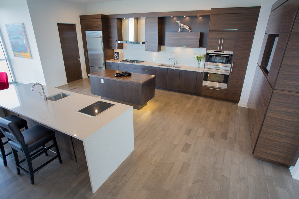 Inspiration for a large contemporary kitchen in Calgary with a double-bowl sink, flat-panel cabinets, dark wood cabinets, white splashback, glass tile splashback, stainless steel appliances, medium hardwood floors and multiple islands.