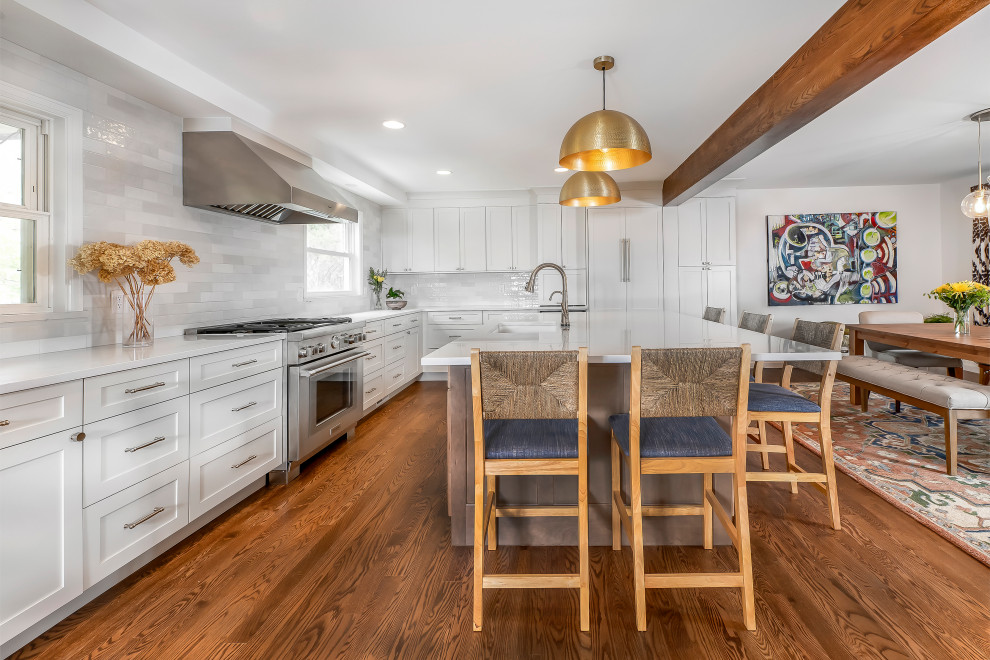 Inspiration for a large transitional l-shaped eat-in kitchen in Denver with an undermount sink, raised-panel cabinets, white cabinets, multi-coloured splashback, subway tile splashback, stainless steel appliances, dark hardwood floors, with island, brown floor, white benchtop and exposed beam.