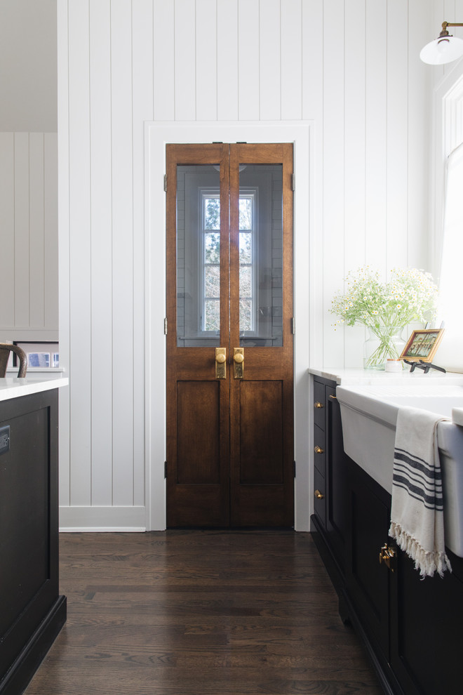Inspiration for a mid-sized transitional l-shaped kitchen pantry in Chicago with a farmhouse sink, shaker cabinets, black cabinets, marble benchtops, white splashback, marble splashback, panelled appliances, medium hardwood floors, with island and brown floor.