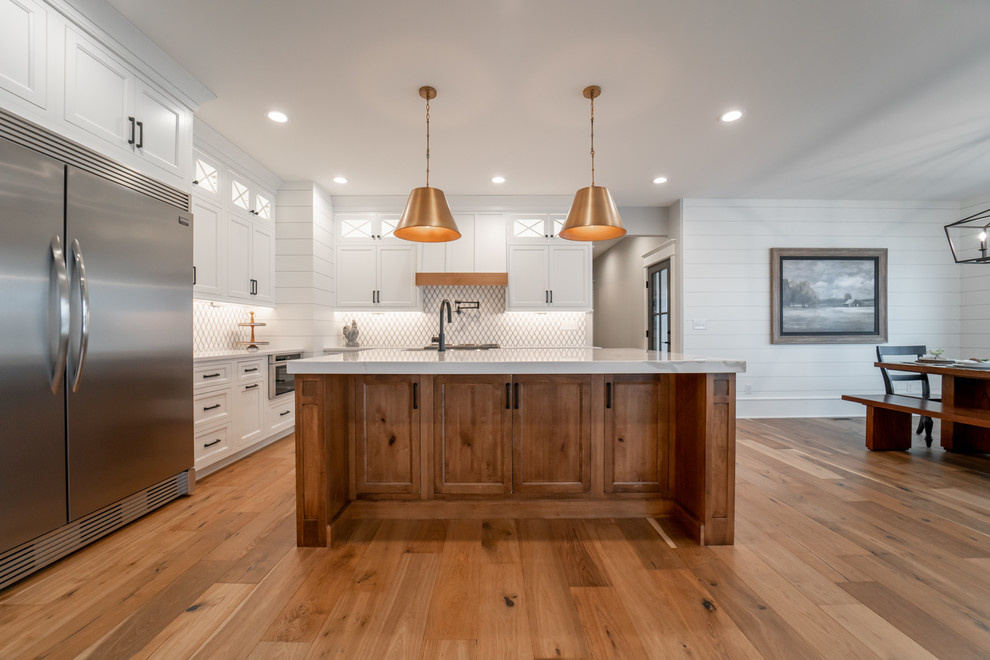 Design ideas for a transitional l-shaped eat-in kitchen in Chicago with shaker cabinets, white cabinets, white splashback, stainless steel appliances, medium hardwood floors, with island, brown floor and white benchtop.
