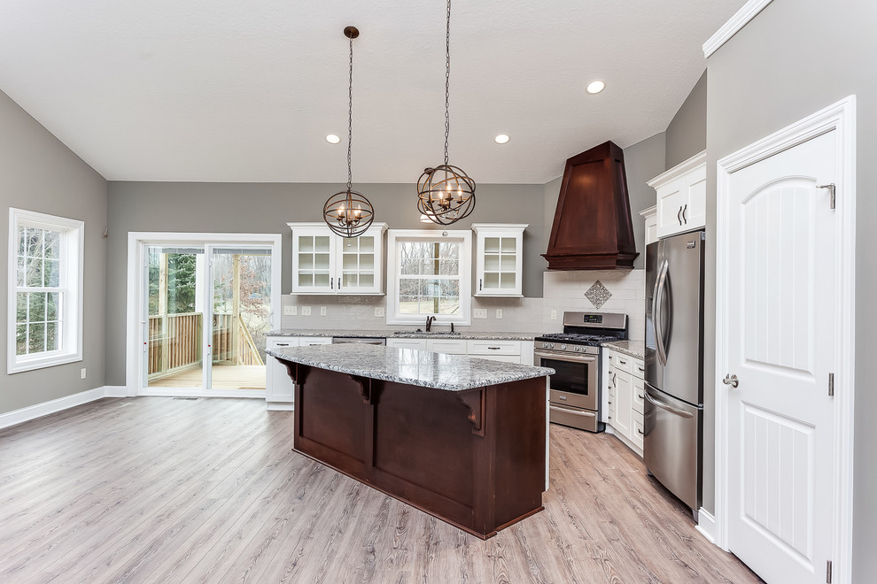 This is an example of a mid-sized transitional l-shaped eat-in kitchen in Cleveland with an undermount sink, shaker cabinets, white cabinets, granite benchtops, beige splashback, ceramic splashback, stainless steel appliances, light hardwood floors and with island.