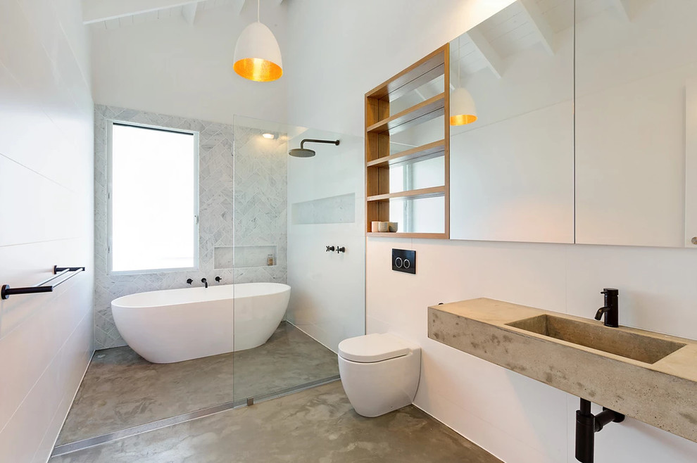 Photo of a contemporary 3/4 wet room bathroom in Other with a freestanding tub, a wall-mount toilet, gray tile, white tile, white walls, concrete floors, a wall-mount sink, concrete benchtops, grey floor, an open shower and grey benchtops.