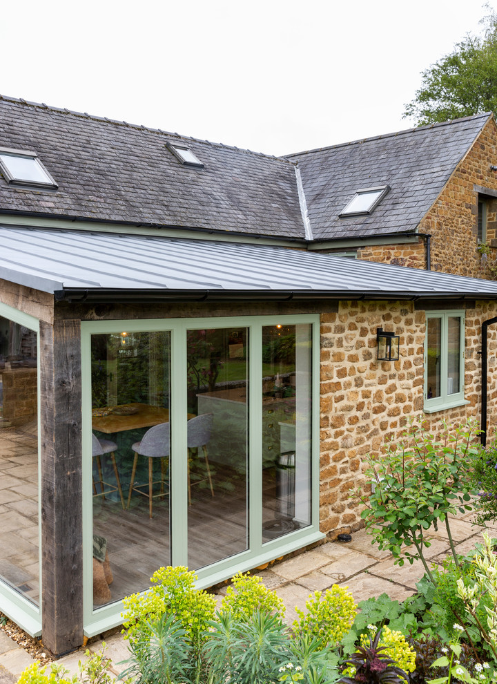 Photo of a country one-storey house exterior in Oxfordshire with stone veneer and a metal roof.