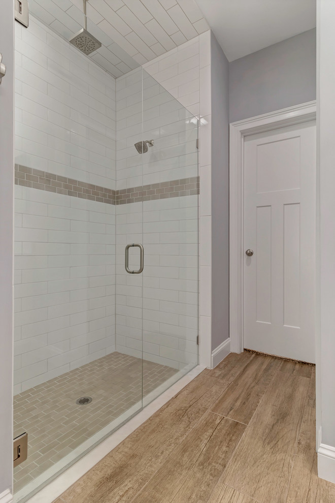 Photo of a large beach style master bathroom in Jacksonville with shaker cabinets, white cabinets, a corner shower, a two-piece toilet, brown tile, ceramic tile, grey walls, light hardwood floors, an undermount sink, quartzite benchtops, brown floor, a hinged shower door and grey benchtops.