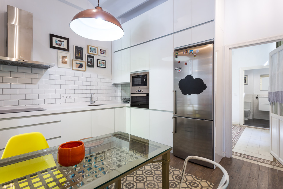 Mid-sized contemporary l-shaped eat-in kitchen in Seville with an undermount sink, flat-panel cabinets, white cabinets, laminate benchtops, white splashback, subway tile splashback, stainless steel appliances, ceramic floors, no island and multi-coloured floor.