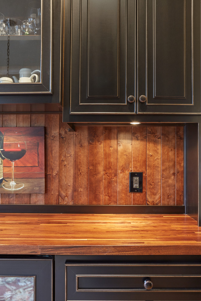 This is an example of a small mediterranean single-wall wet bar in Atlanta with an undermount sink, raised-panel cabinets, black cabinets, wood benchtops, brown splashback and light hardwood floors.